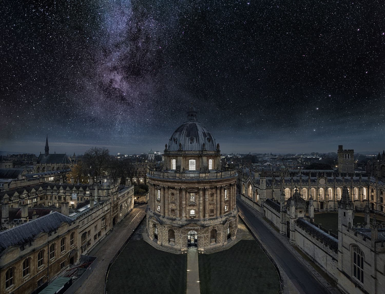L'immagine mostra una veduta aerea notturna della Radcliffe Camera, parte della Bodleian Library dell'Università di Oxford, con un cielo stellato e la Via Lattea visibili sullo sfondo.