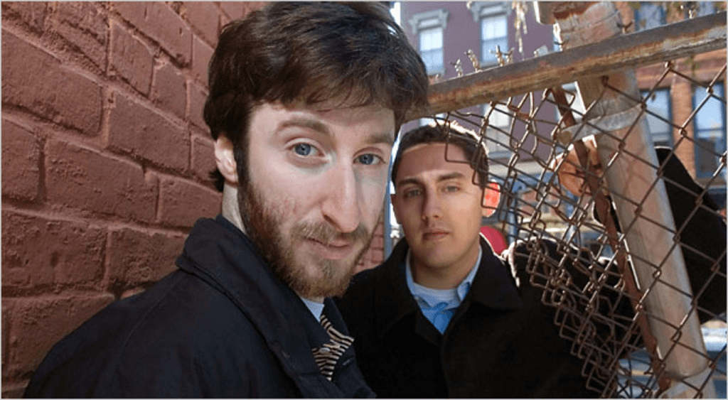 L'immagine mostra Holden Karfnosky e un giovane in piedi davanti a un muro di mattoni rossi; uno è in primo piano e guarda direttamente nella fotocamera, mentre l'altro è dietro, leggermente sfocato.