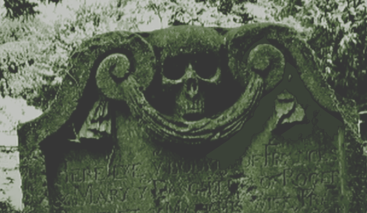 L'immagine mostra un'antica lapide consumata dal tempo con un teschio scolpito sulla sommità e un testo illeggibile a causa dell'usura.