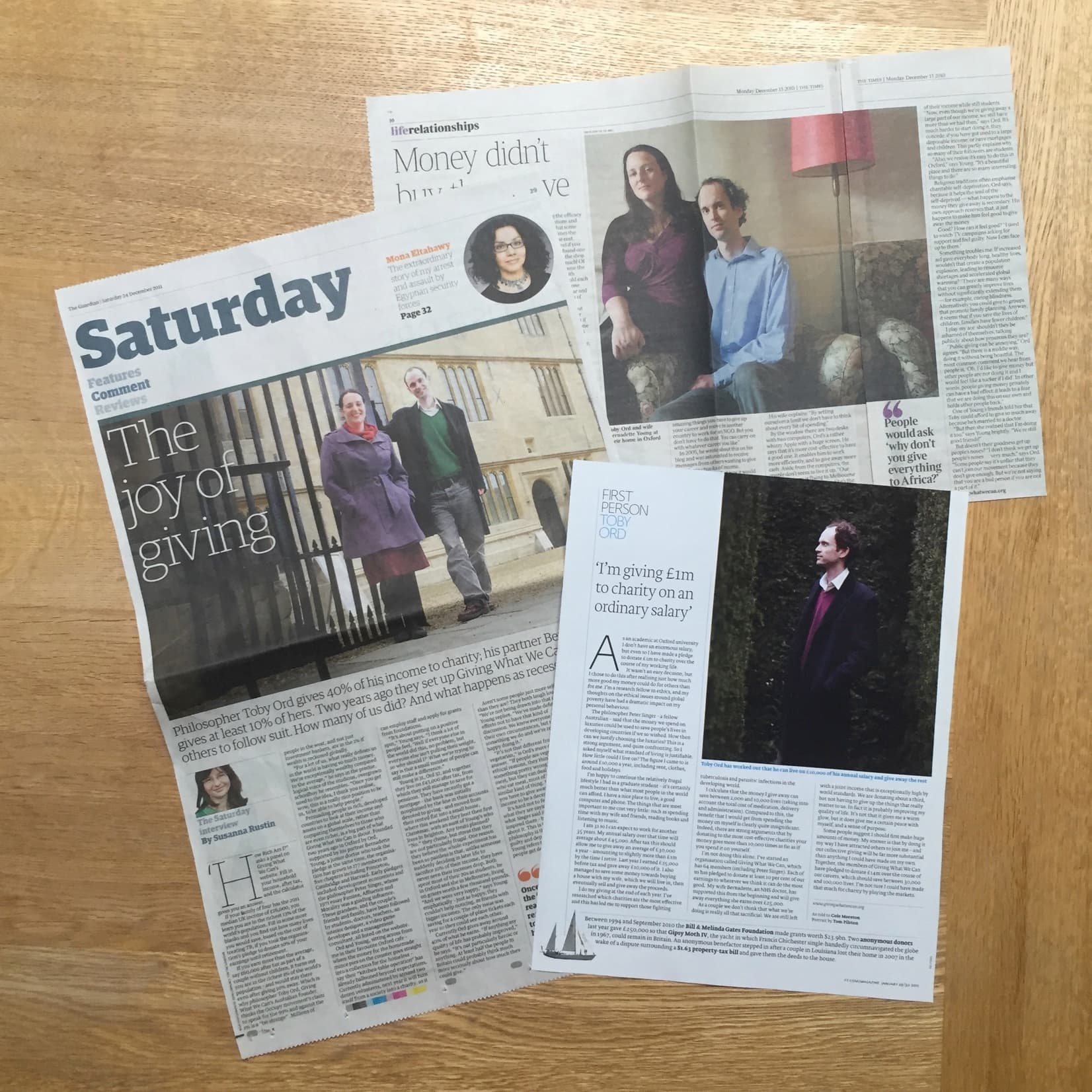 L'immagine mostra diverse pagine di un giornale sparse su una superficie di legno, con articoli che trattano di organizzazione di beneficenza.